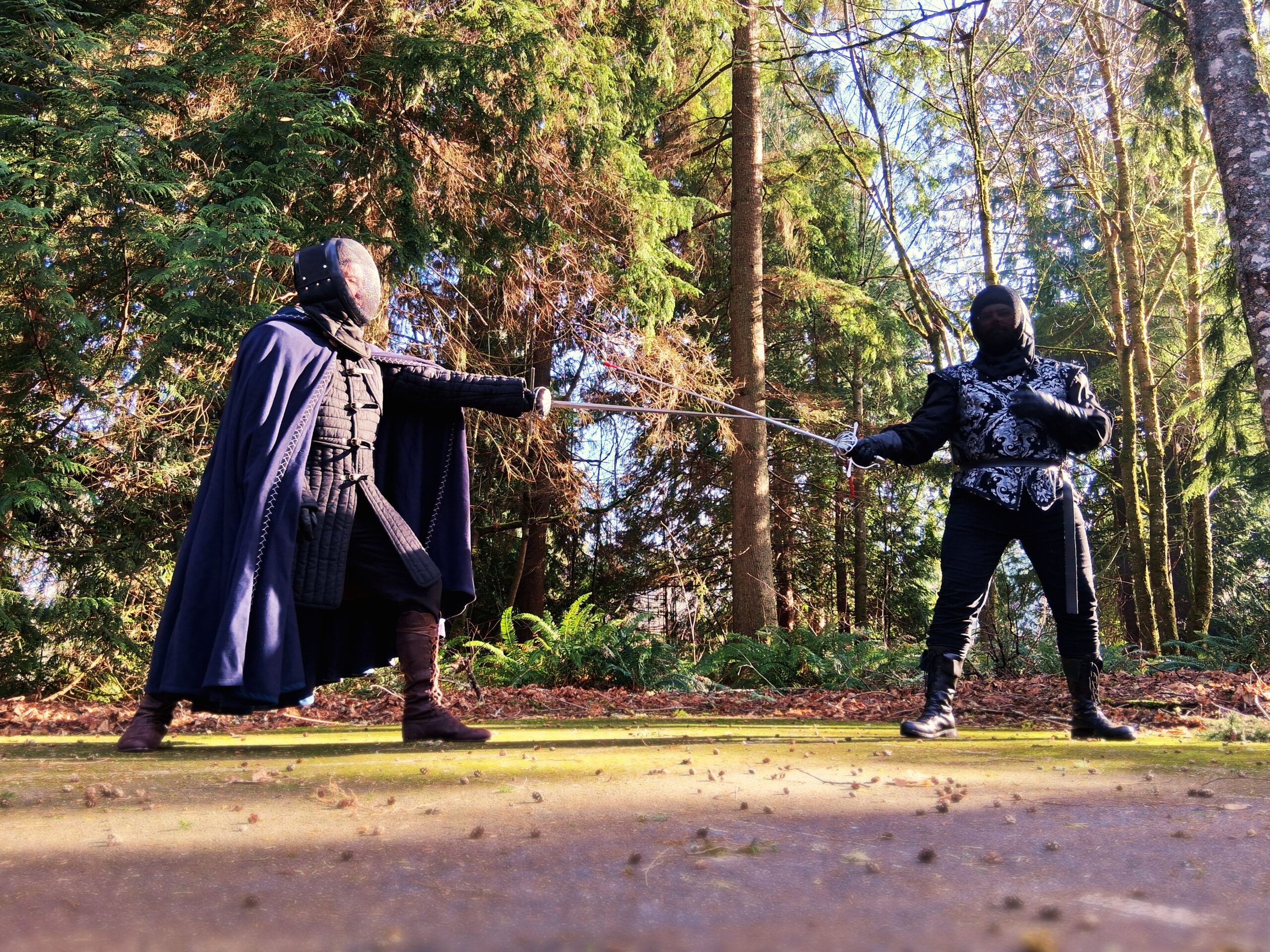 A pair of rapier fighters in full garb begin a bout with swords crossed.